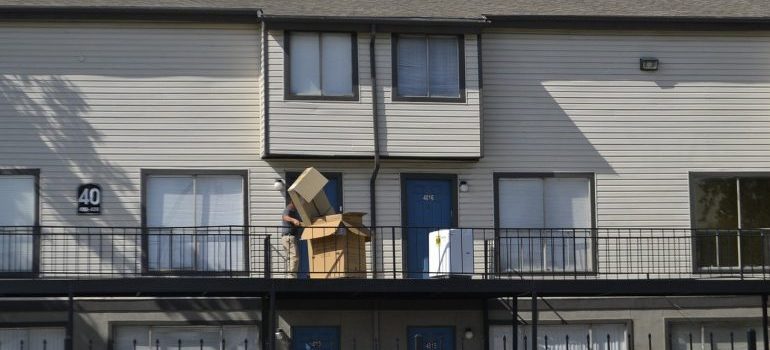 A person carrying stacked cardboard boxes along an apartment balcony during a move