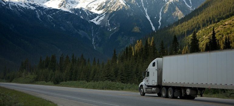 A white semi-truck with a cargo trailer driving on a mountain highway