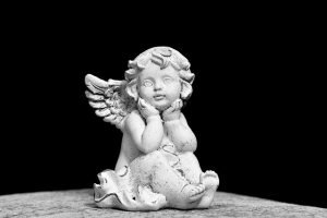 Small white angel figurine with wings resting its chin on its hands