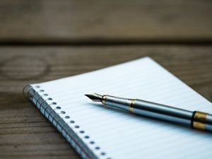 Fountain pen resting on a blank spiral notebook on a wooden table