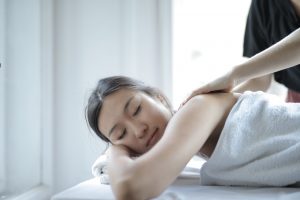 A woman lying on a white massage table getting a back massage from a masseuse.