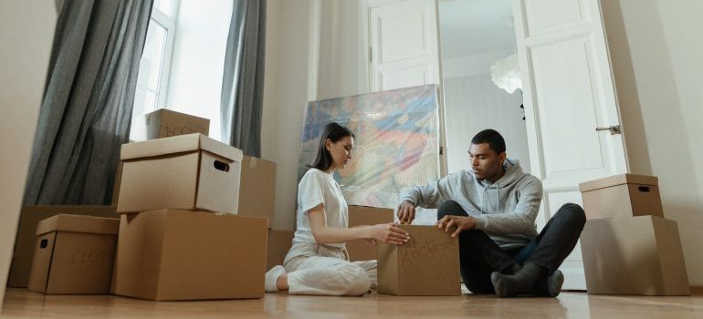 Couple sealing moving boxes on the floor with a large abstract painting leaning against the wall behind them