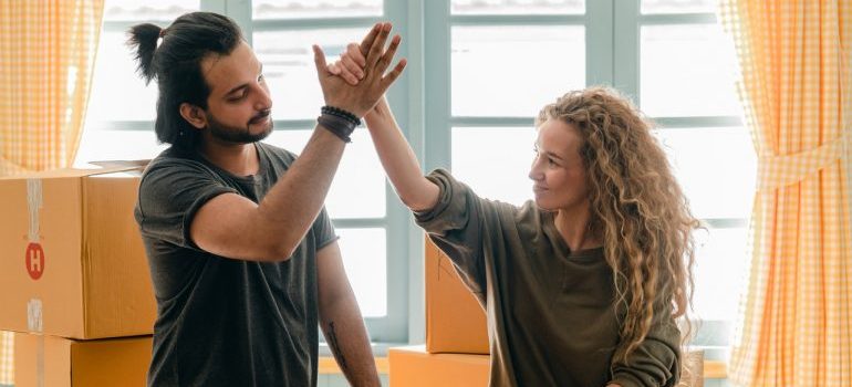 Couple giving each other a high five among packed cardboard moving boxes