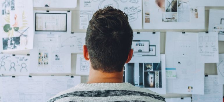 Man looking at a wall covered with pinned sketches and notes while planning a move from Mississippi to Tennessee