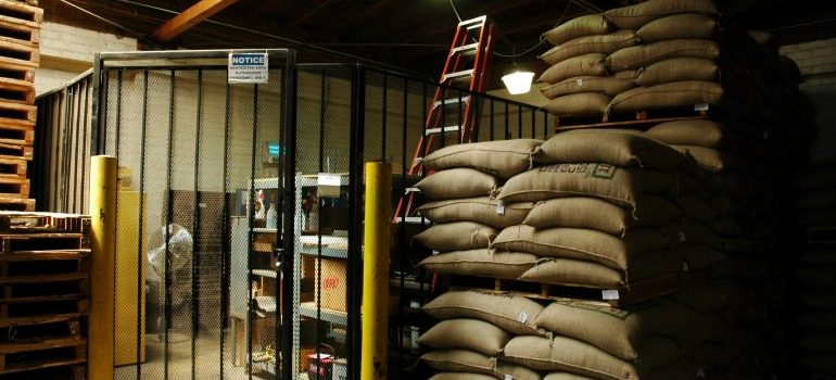 Sacks of goods stacked on pallets next to a caged storage area inside a warehouse