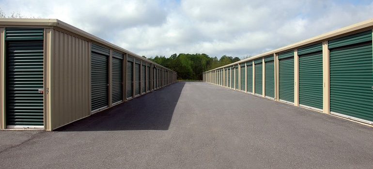 Two rows of drive-up storage units with green roll-up doors along a paved lane