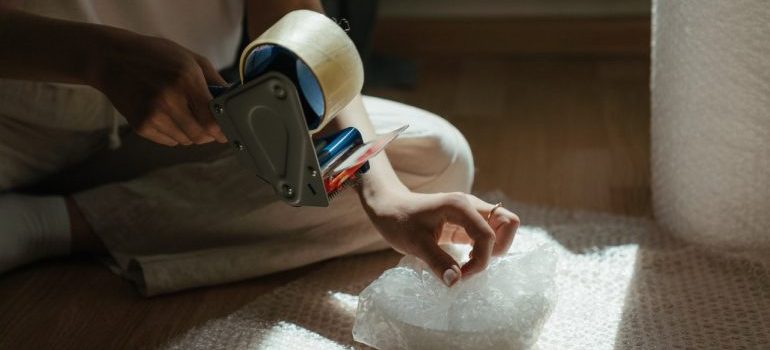 A woman sealing a moving box with packing tape, one of the packing materials on her checklist