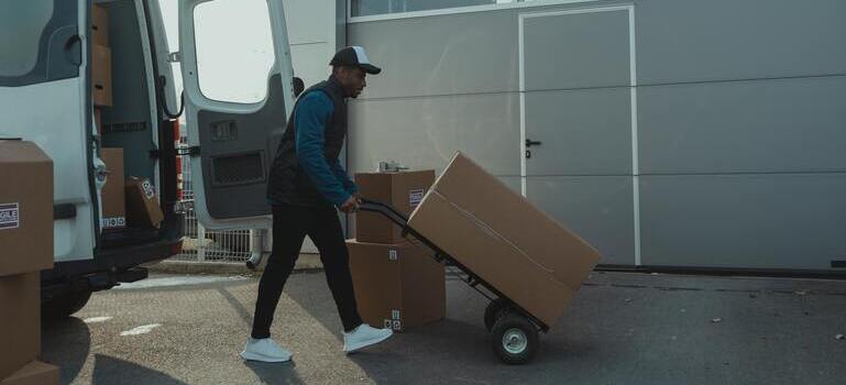 Mover pushing a hand truck stacked with boxes toward an open moving van