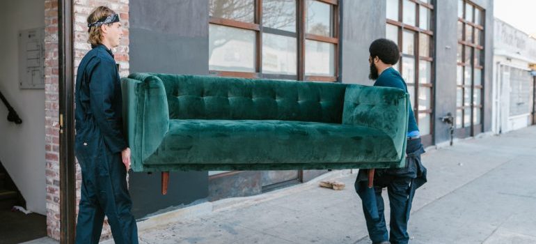 Two movers carrying a couch out of a home