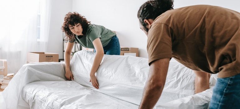 Couple pulling a white plastic cover over a fabric sofa before a move