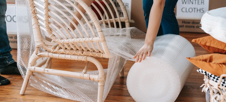 Person wrapping a rattan armchair in bubble wrap from a large roll