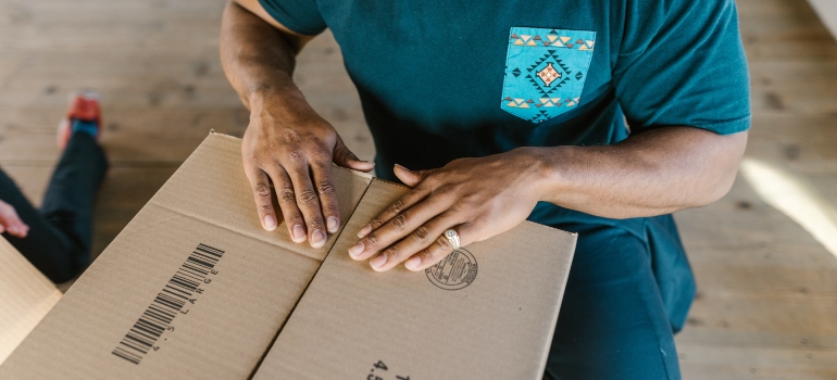 A mover pressing down the flaps of a cardboard box, the last step of packing a mirror
