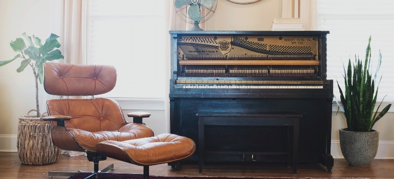 A black upright piano near a leather chair, ready for the steps to packing a piano for relocation