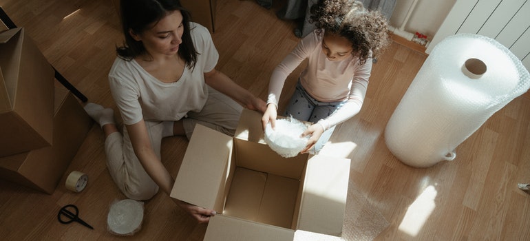 Woman in Gray Shirt Sitting on Floor Beside Girl in White Shirt.