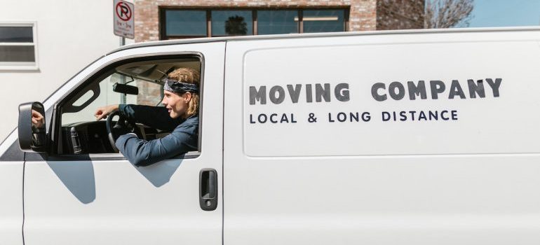 Smiling mover at the wheel of a white van marked moving company, local and long distance
