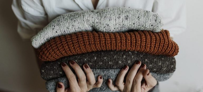 A woman holding a stack of folded sweaters