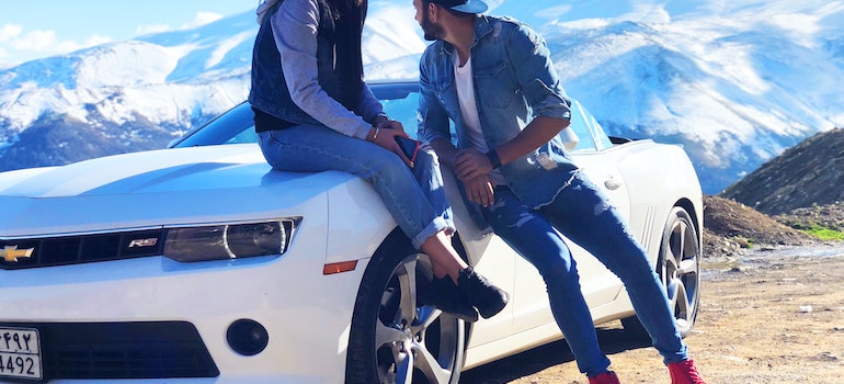 A young couple sitting on the hood of a car outdoors