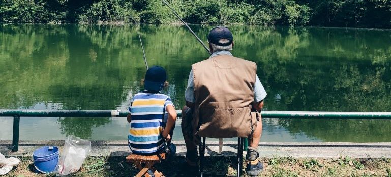 A boy and his grandfather fishing from the shore of a lake