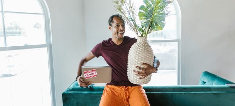 Smiling man holding a plant and a box, moving to one of the best places in Colorado for a fresh start after divorce