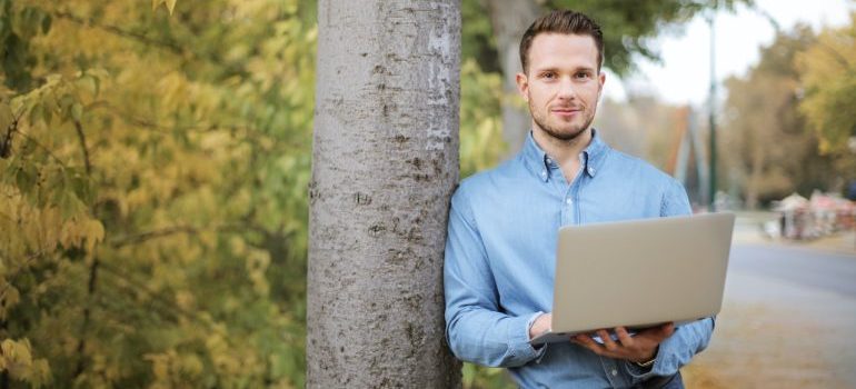 A man leaning against a tree with a lap top