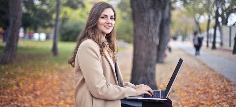 Woman working on a laptop on a park bench surrounded by autumn leaves