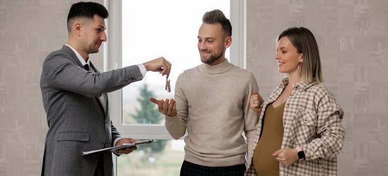 A real estate agent handing house keys to a couple after they bought a home in one of the cities in Colorado where you can live on a budget
