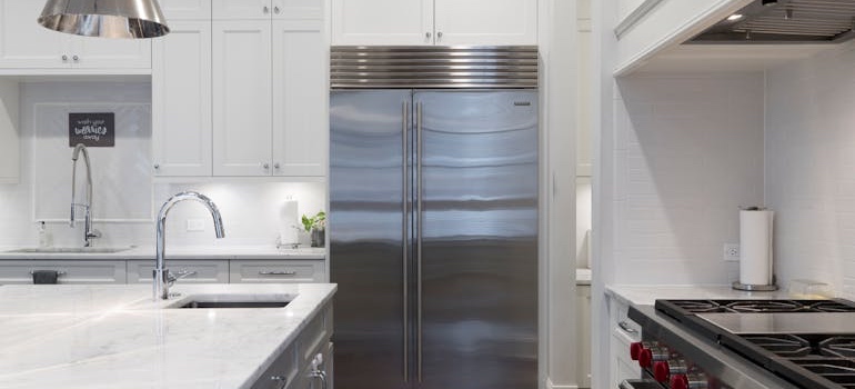 A stainless steel French-door refrigerator in a white kitchen next to a gas range