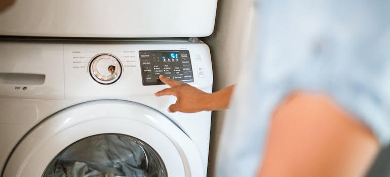A person pressing the control panel of a white front-load washing machine before preparing it for a move
