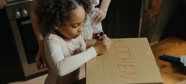 Two people labeling cardboard moving boxes as they create an inventory system while packing