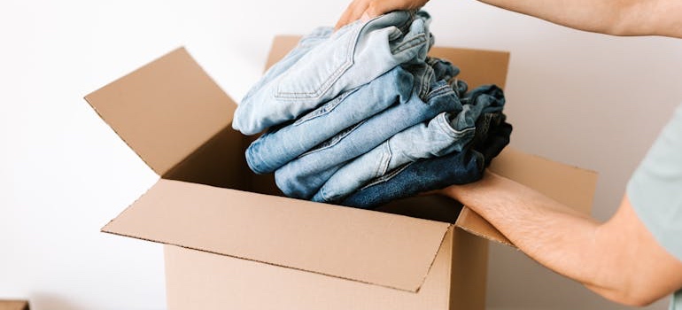 A person packing folded jeans into a moving box