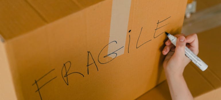 A person writing the word ‘fragile’ on a moving box