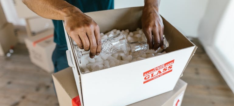 A person wrapping drinking glasses in paper and packing them into a box