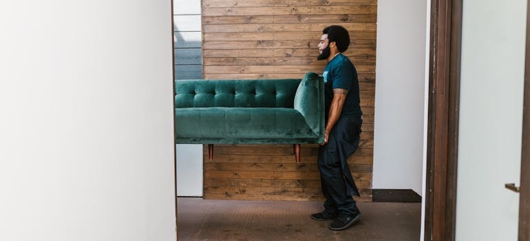 A mover carrying a sofa wrapped for a move