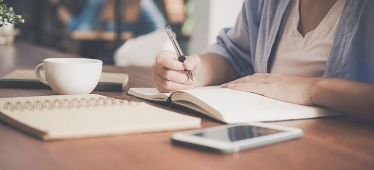 A person writing an inventory list in a notebook for preserving family heirlooms and antiques in storage