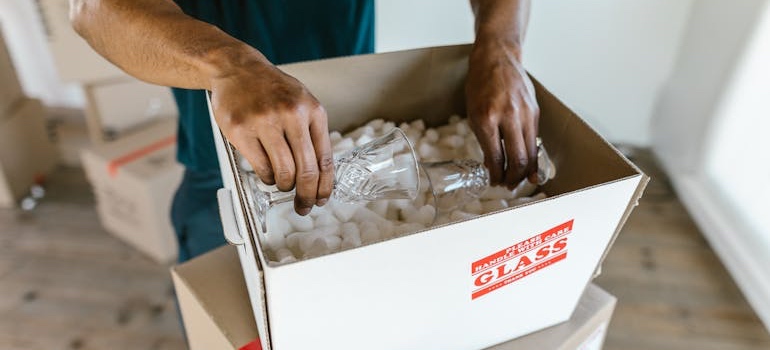 A person packing drinking glasses into a box with shockproof packing materials and techniques