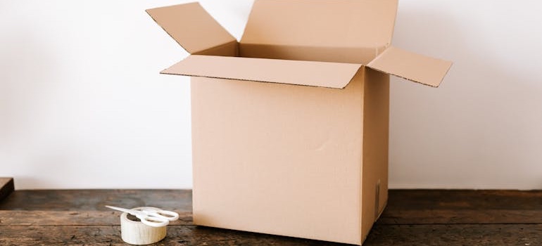 An open cardboard box with tape and scissors on a wooden table
