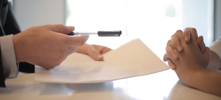 A person handing over a document and pen across a desk