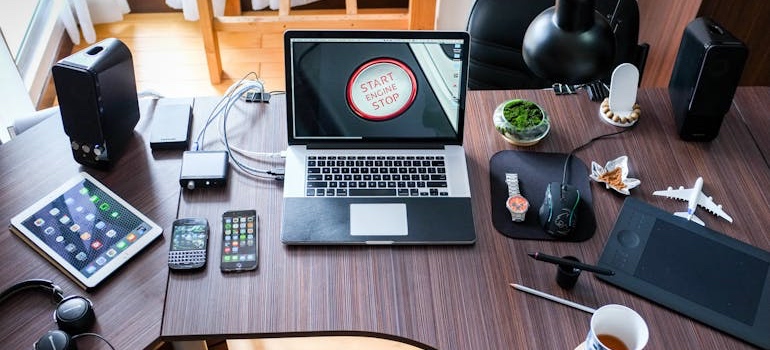 Laptop, tablet, phones and speakers on a wooden desk