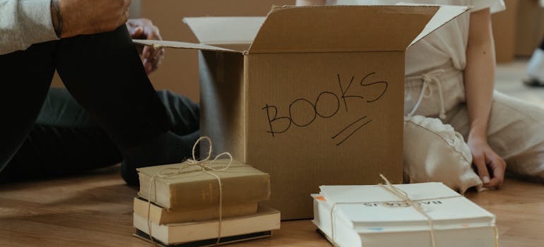 Two people packing books into a cardboard moving box