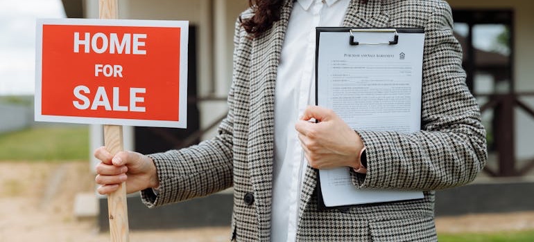 A real estate agent holding a 'for sale' sign