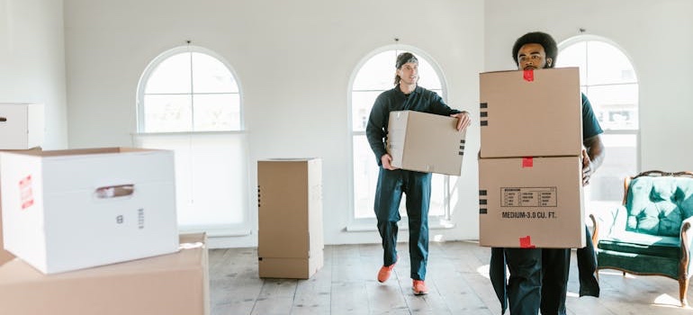 Two movers carrying moving boxes into a new home
