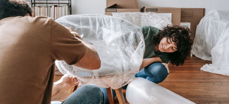 A couple wrapping a chair in protective material before storing furniture long-term
