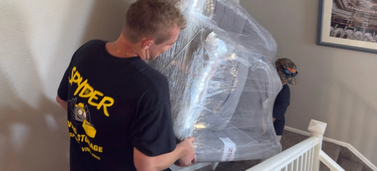 Castle Rock CO movers from Spyder carrying a wrapped piece down a staircase