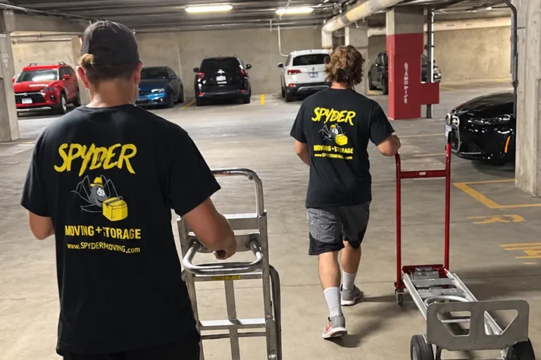 Two Spyder movers pushing dollies through a parking garage
